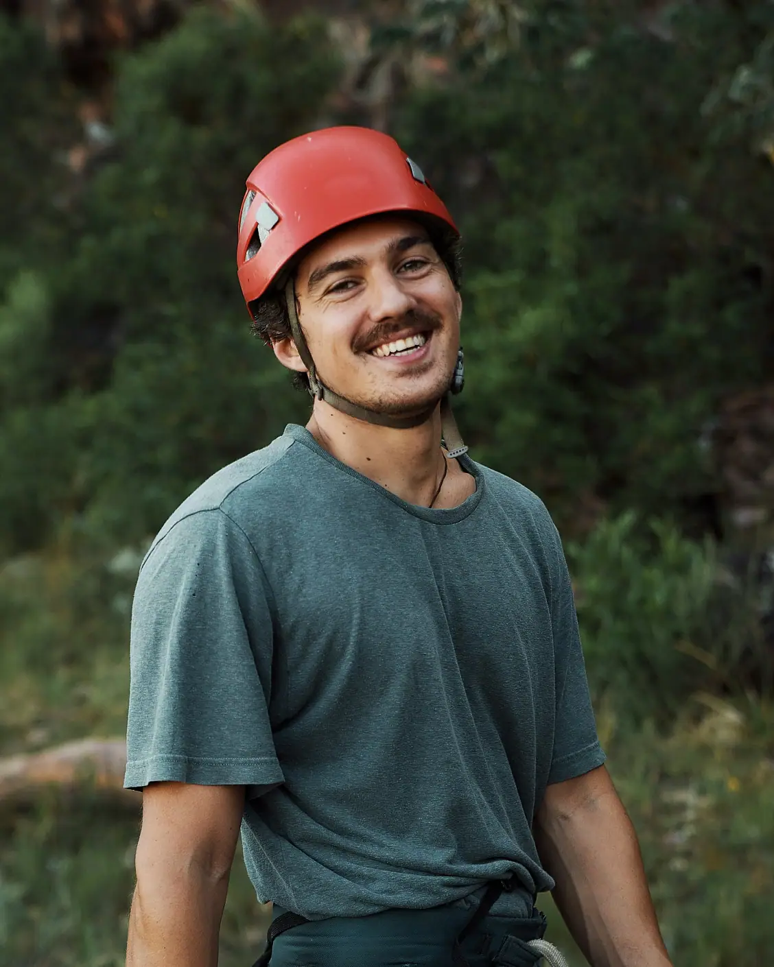 Un grimpeur souriant portant un casque rouge à l’extérieur.