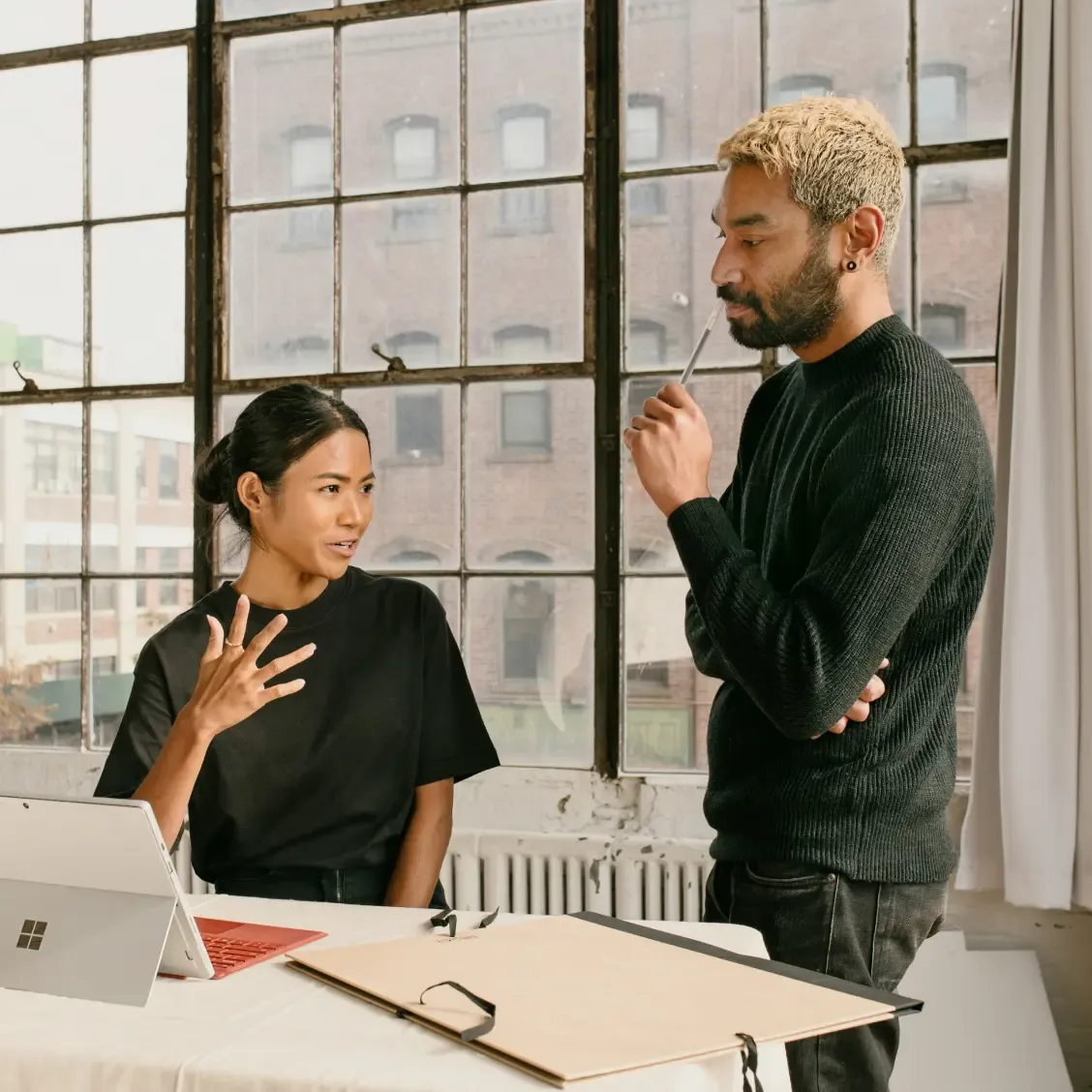 Deux collègues debout près d’un bureau discutent des avantages dans un espace lumineux.