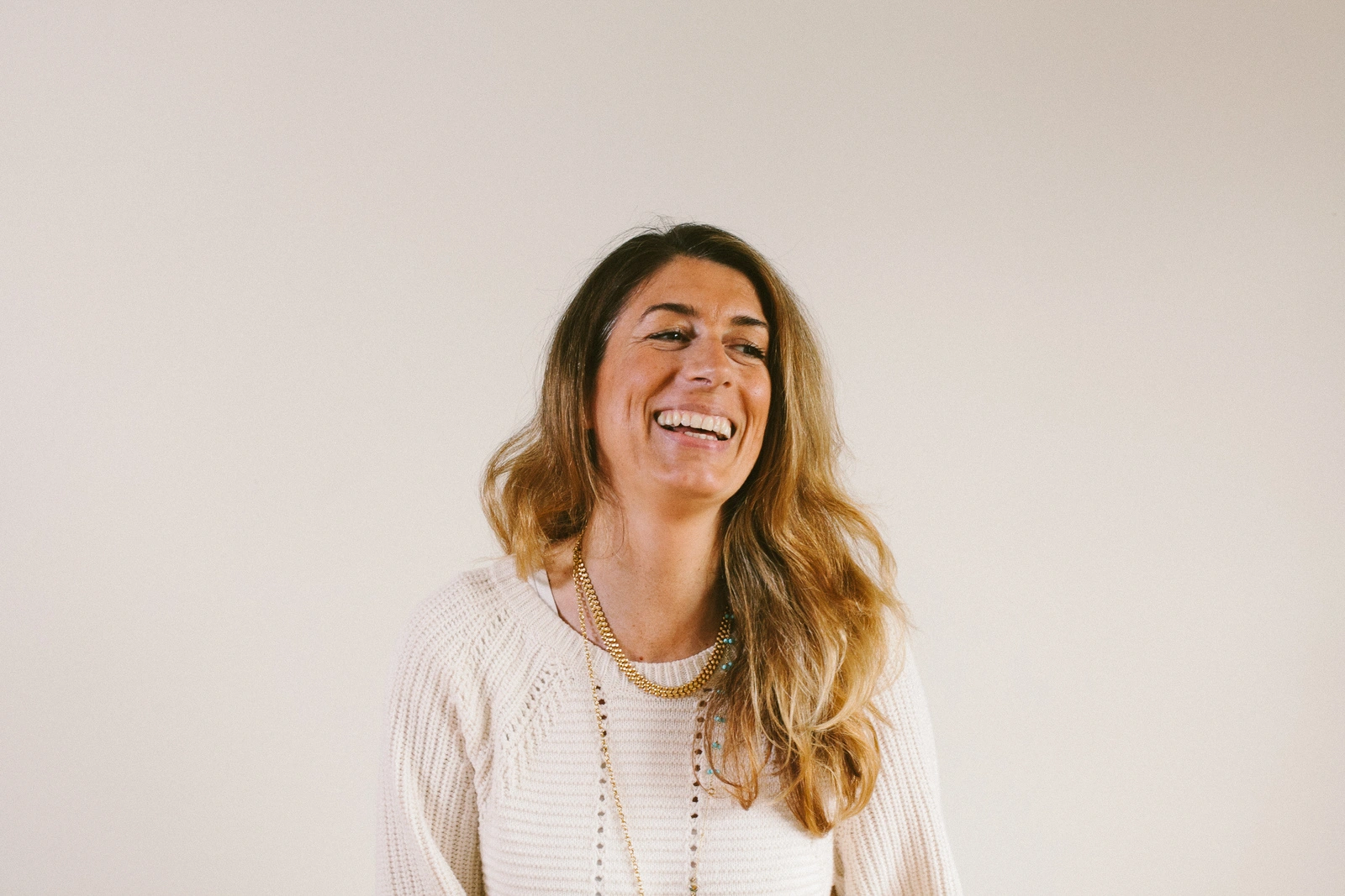 Smiling person with long hair, wearing a cream sweater.
